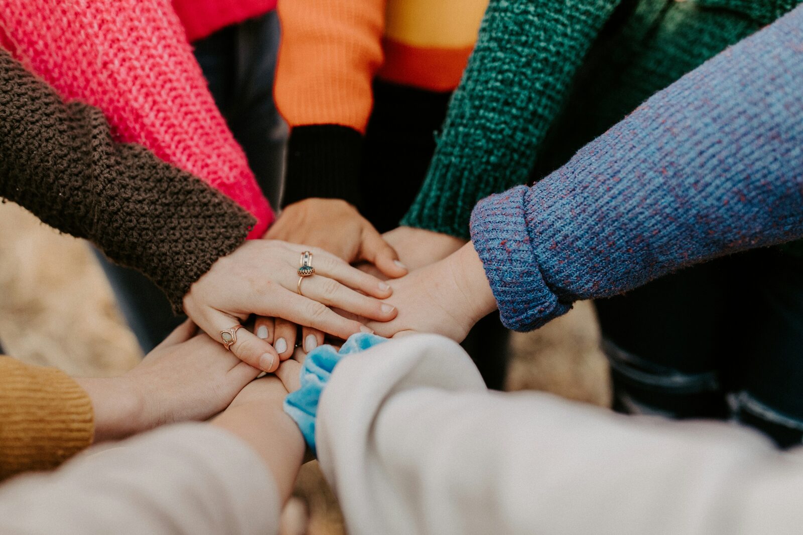 A diverse group of people in colorful sweaters stacking their hands together in unity